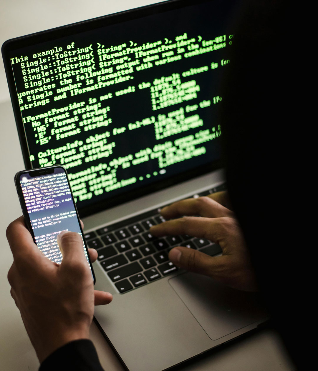 Unrecognizable hacker with smartphone typing on laptop at desk<br />
Conspiracy and fraud